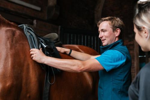 Man checking the fit of a saddle on a horse